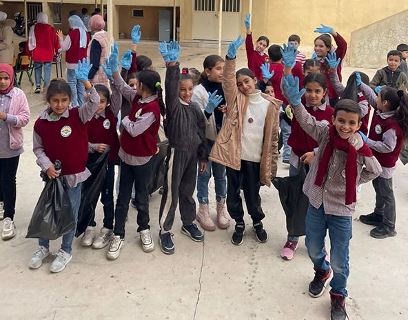 young school children standing outside a building and raising their hands