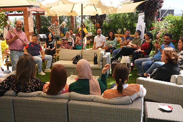 People sitting outside in patio chairs in a circle listening to a man speak