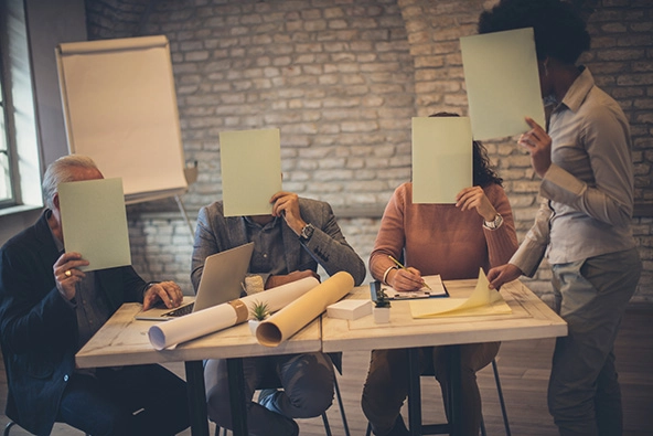 people around a table hiding behind paper