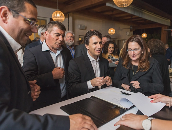 Men and women in business attire standing around a table with papers to sign.
