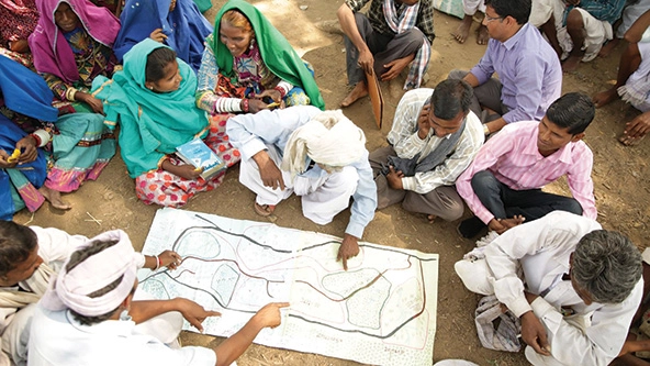 group of people seated on ground looking at large map