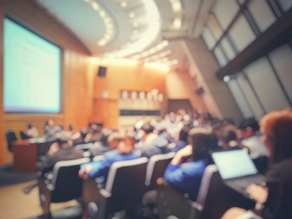 Blur of auditorium room with screen at front and people sitting in rows of seats