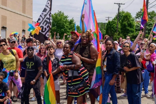 A gathering of people carrying trans and LGBTQ pride flags.