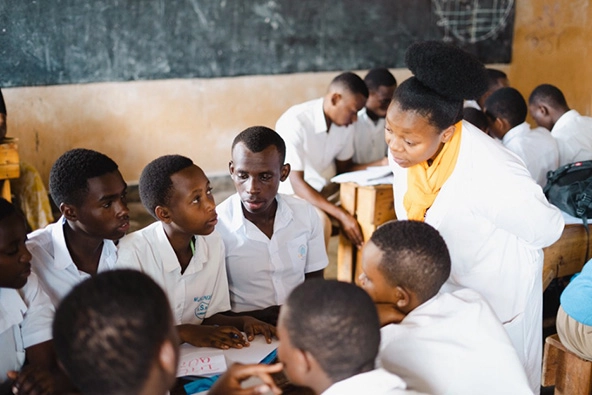 A woman stands over a group of students in a classroom