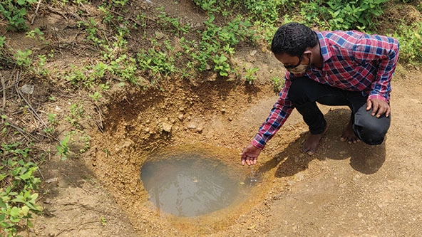 Man pointing to a small dug-out well in the ground