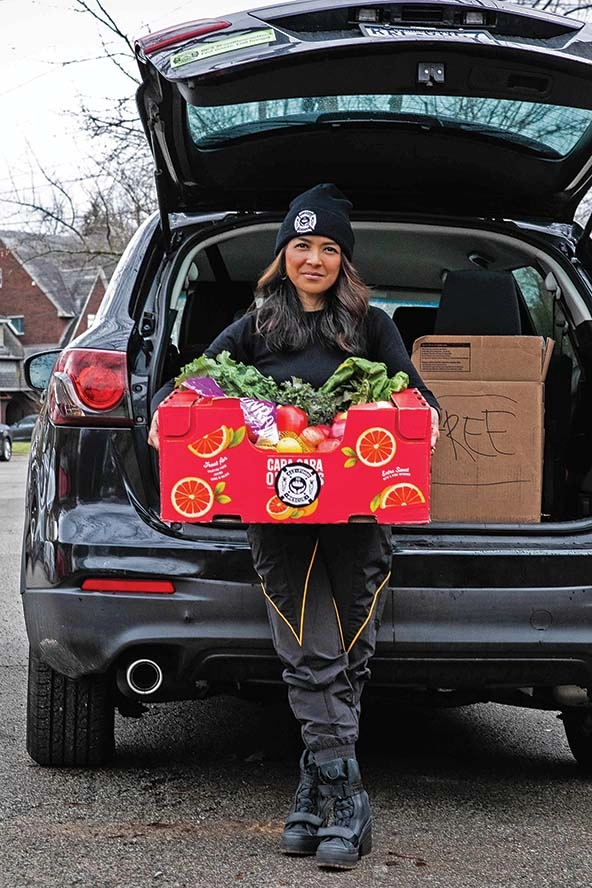 Woman standing in front of an SUV's open hatch holding a box of produce