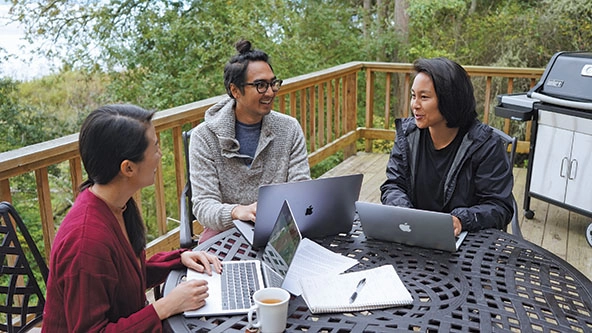 Three people sitting at a table with laptops.