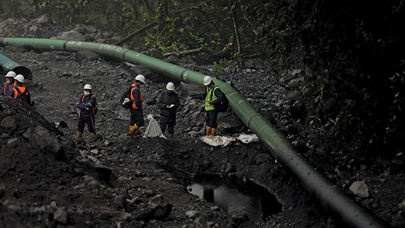Workers in hardhats, face masks, and orange vests stand near a ruptured oil pipeline in the Amazonian region of Ecuador.