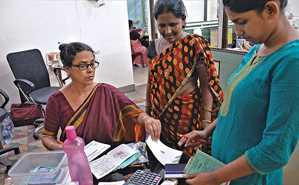 Three Indian women at a table with calculator, papers, and savings books.