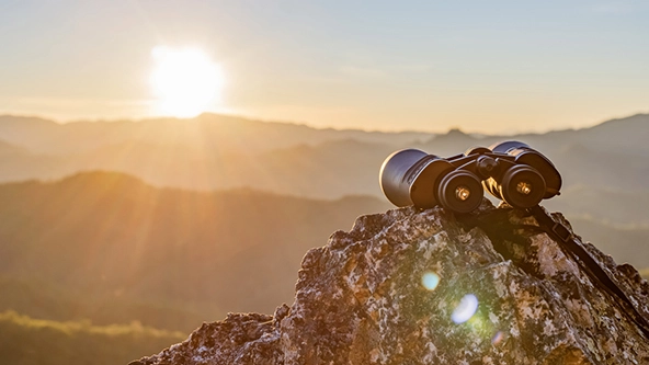Binoculars on top of rock mountain at beautiful sunset background