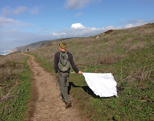 Man walking down a path sweeping the area for ticks with a white cloth attached to a wooden dowel