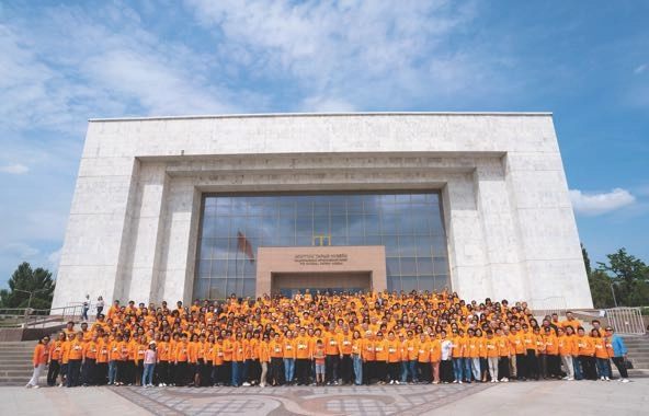 a crowd of people in orange shirts, arranged in rows, in front of the Kyrgyz State History Museum