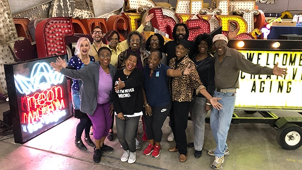 Older adult participants, teaching artists, and museum staff pose together with arms outstretched