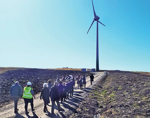 People walking on a path toward a wind turbine.