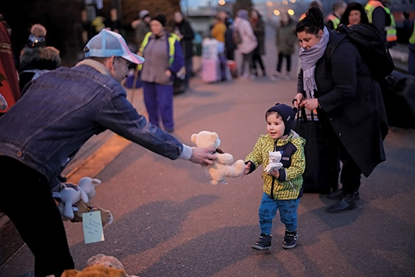 A person handing a teddy bear to a small child.