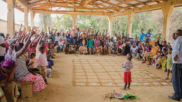 People sitting in a pavilion raising hands to take a vote