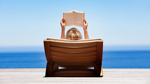 Rear view of woman reading outdoors in wooden chair next to water