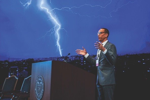 Otho Kerr of the Federal Reserve Bank of New York stands at a podium and gives a speech while lightning is visible in the background