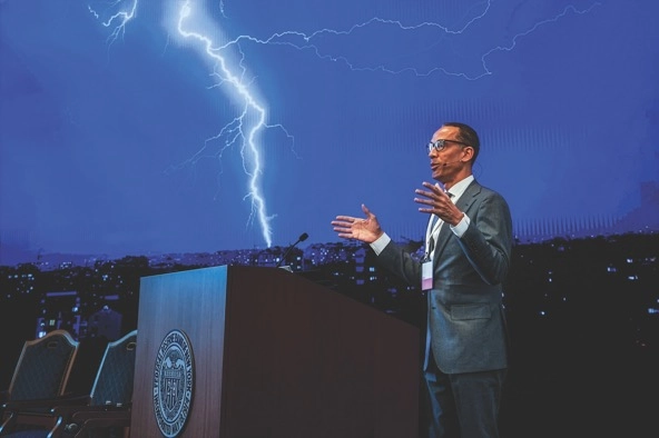 Otho Kerr of the Federal Reserve Bank of New York stands at a podium and gives a speech while lightning is visible in the background
