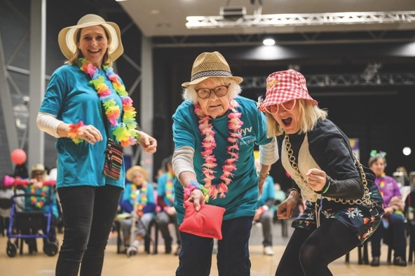 an elderly woman throws a bean bag while two other women cheer her on