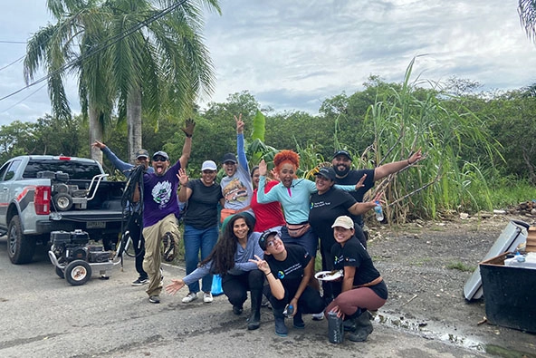 A group of volunteers outside with a palm tree and cloudy skies smiling, looking at the camera