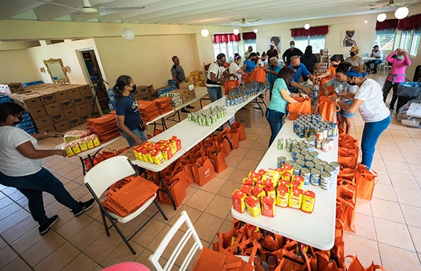 volunteers standing at long tables filling orange bags with canned food