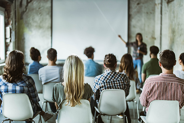 Rear view of large group of creative people facing a teaching and screen