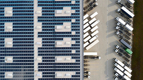 [aerial view of semi trucks next to warehouse with solar panel array on roof]
