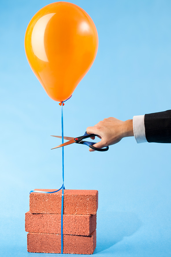 Orange balloon tethered to three red bricks, scissors cutting string stock