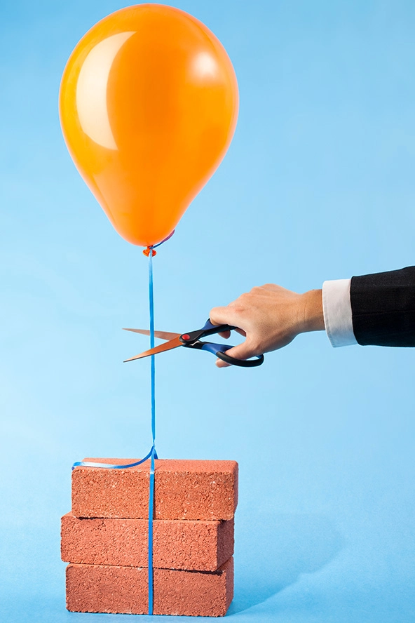 Orange balloon tethered to three red bricks, scissors cutting string stock