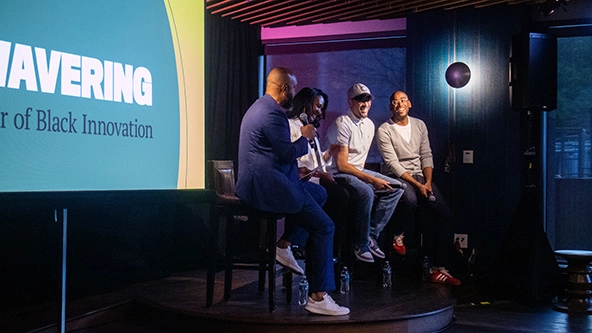 Four people sitting on stools having a conversation in front of an audience