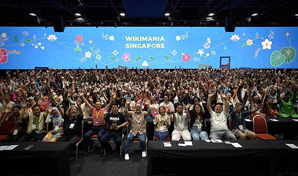 Photo of a large crowd of people seated and cheering in a conference room