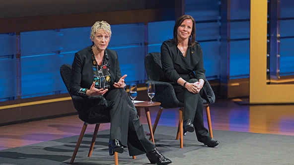 Two women sitting in chairs on a stage.