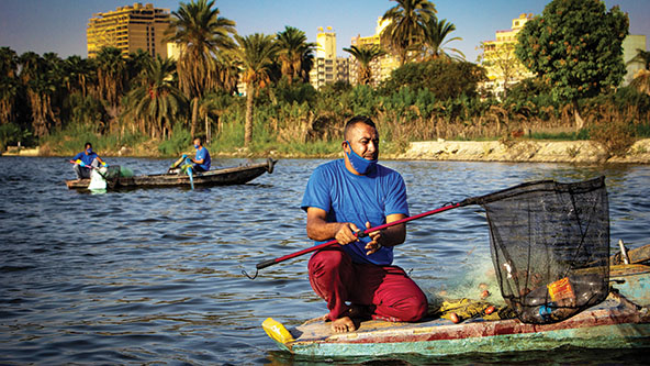 A man uses a fishing net to pull garbage from a river
