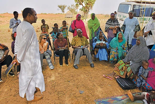 Group of people sitting and standing outside at a meeting in Niger.