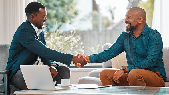 Two men sitting in chairs at a table and shaking hands