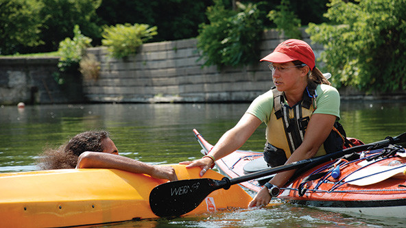 Woman in a kayak helps person next to a flipped kayak in water