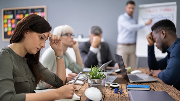 Upset businesspeople sitting at a table while colleague gives presentation