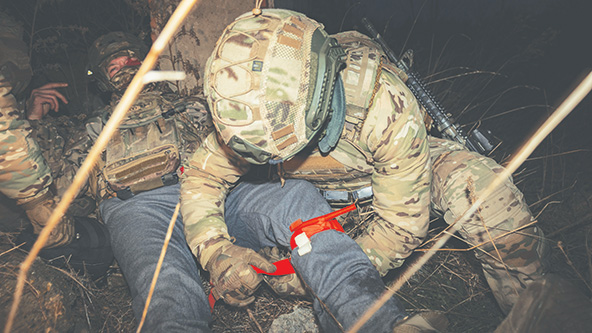 Soldier applying a tourniquet to another soldier laying on the ground