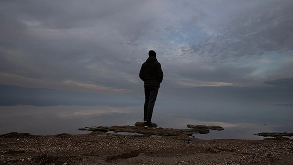 lonely man with overcast sky at water's edge