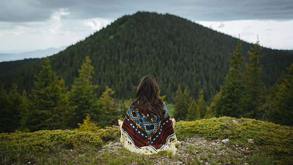 Woman with poncho meditating in the mountain at sunset